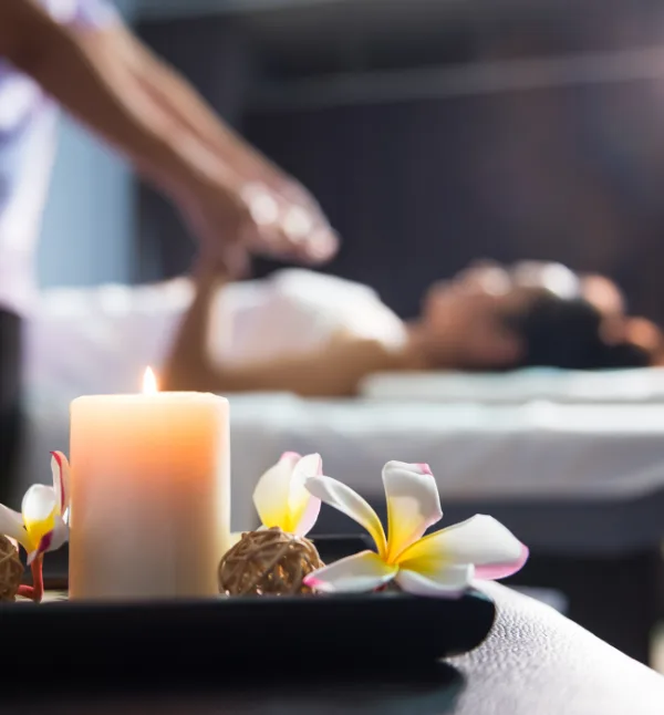 Candle and frangipani flowers with massage therapy in the background